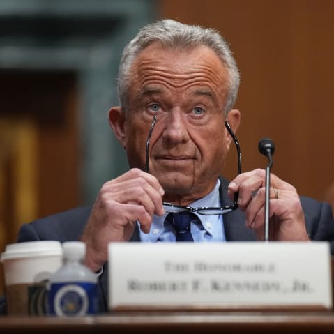 RFK Jr. raises his eyebrows with his glasses in his hands.