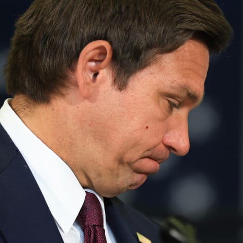 Ron DeSantis, seen in profile, bites his lips with his head down.