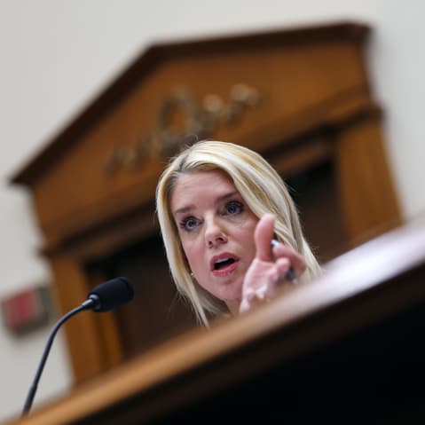 Pam Bondi behind a microphone, partially obscured by the desk in front of her.
