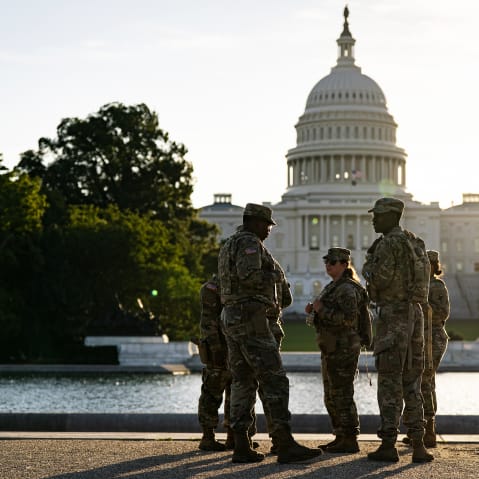 Several National Guard members stand by a pond across from the Capitol at sunset.
