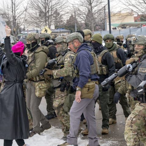 There is one single protestor wearing a a pin k hat in the left side of the frame confronting a large number of federal agents.