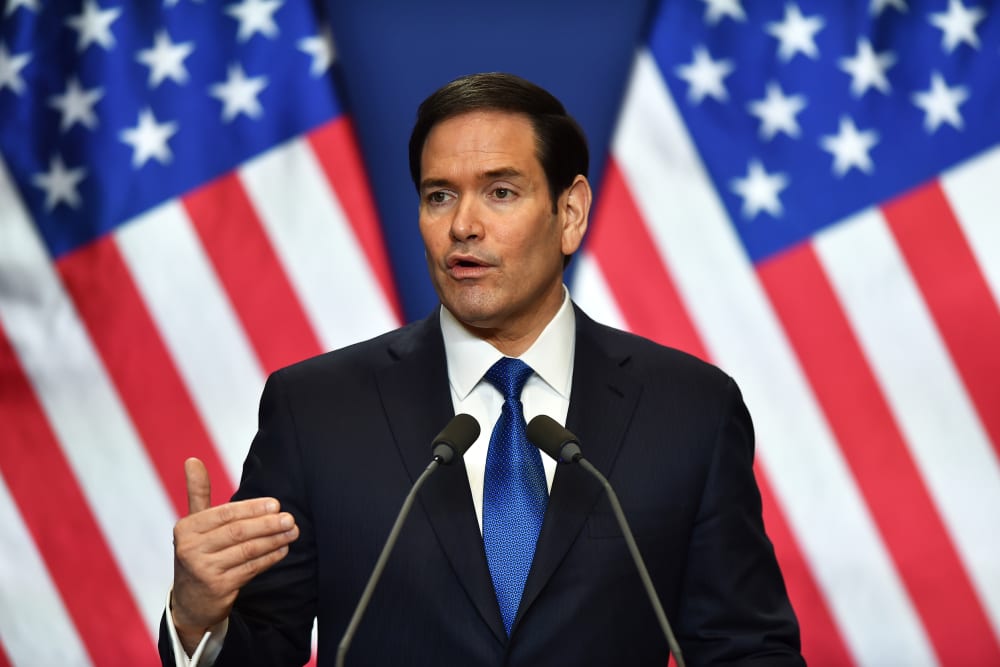 Marco Rubio is seen speaking in front of two US flags.
