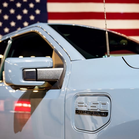 A Ford Motor Co. F-150 Lightning EV in front of an American flag.