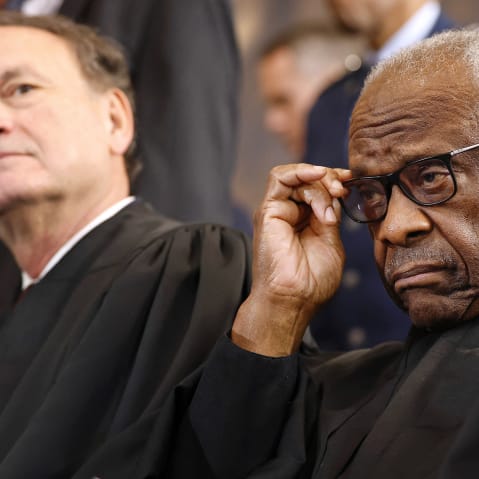 Clarence Thomas adjusts his glasses as Samuel Alito leans back in the background.