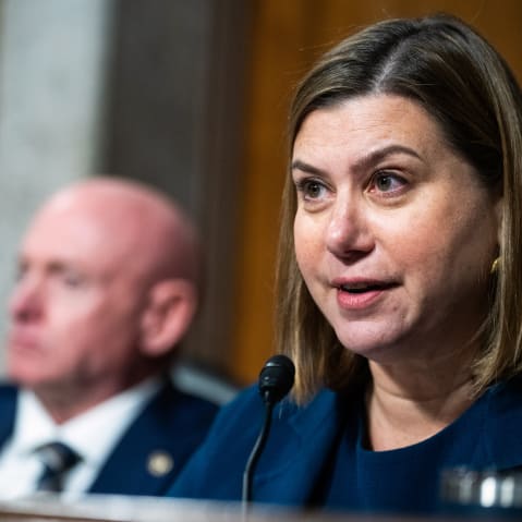 Elissa Slotkin, right, speaks into a microphone. Mark Kelly is out of focus behind her and to her left.