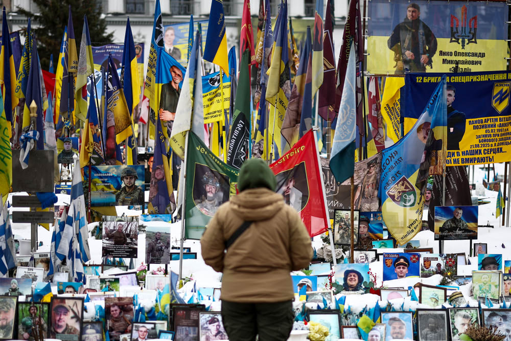 A person stands in front of photos and flags in a memorial.