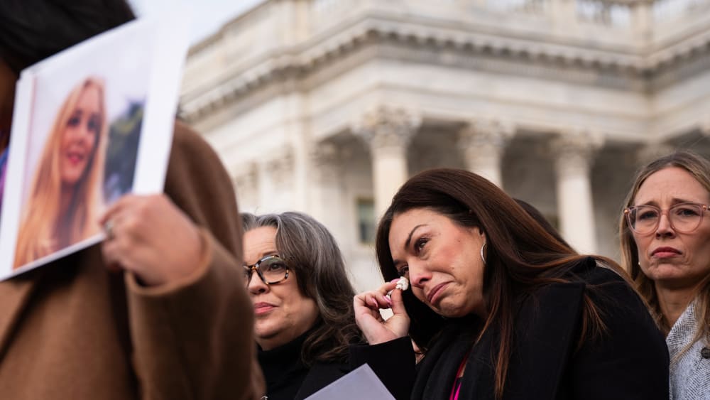 Epstein survivor Haley Robson, second from right, wipes tears from her eyes with tissue. She is surrounded by people, including other survivors.