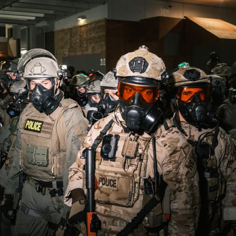 A crowd of federal officers in gas masks and helmets.