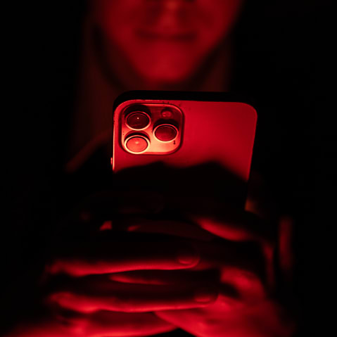 A person's hands hold an iPhone. The scene is bathed in a red light.