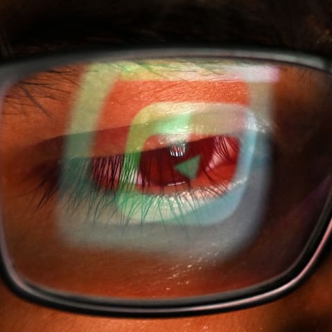 The YouTube logo is reflected in one lens of a person's glasses.