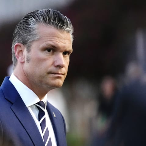 Pete Hegseth looks on on the side left side of the frame, his surroundings are out of focus.