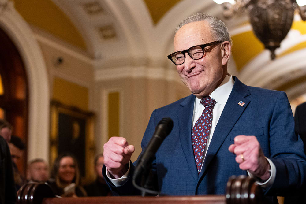 Chuck Schumer pumps his fists in excitement behind a podium.