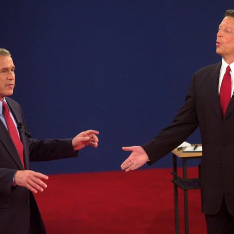 George Bush speaks to Al Gore while Gore reacts by opening both arms.