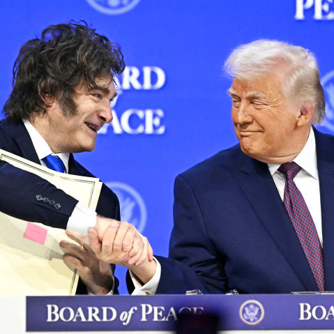 Javier Milei , left, shakes hands with Donald Trump while sitting at a table.