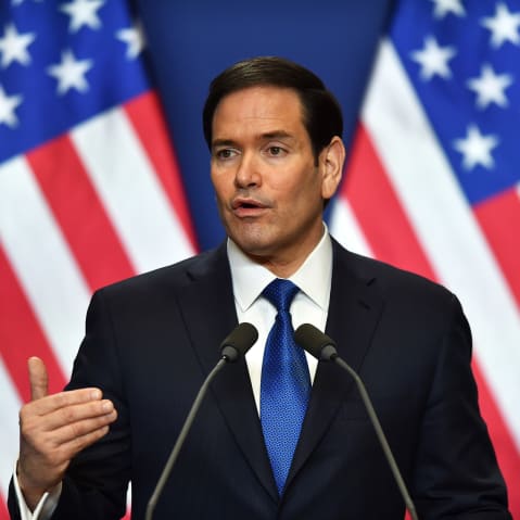 Marco Rubio is seen speaking in front of two US flags.