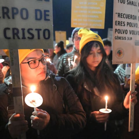 Two women hold candles and signs during a this outdoor Ash Wednesday Mass.