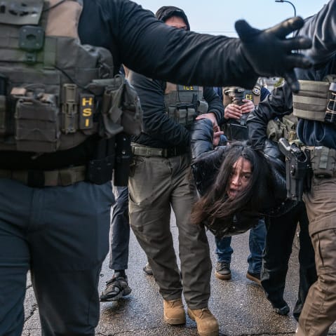 Federal agents hold a person by their arms and legs in the street.