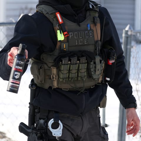 Torso of an ICE agent is seen as he aims a pepper spray canister forward.