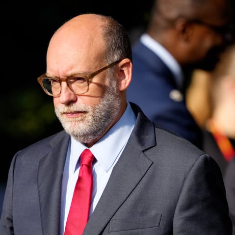 Russell Vought walks in daytime, followed by other people.