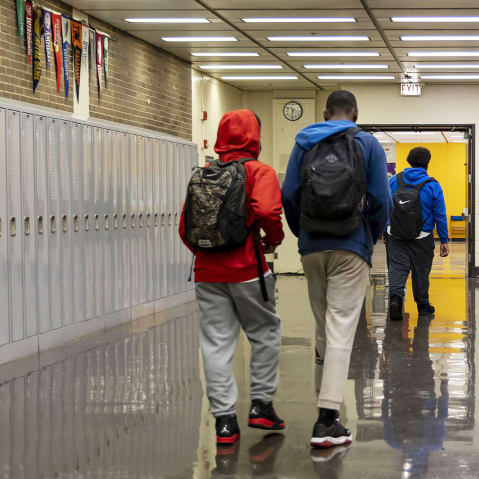 Three students seen from behind as they walk down a high school hallway.