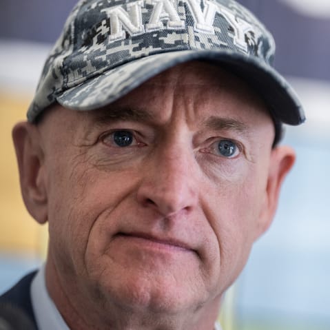 Arizona Sen. Mark Kelly looks on at an event, wearing a Navy cap.
