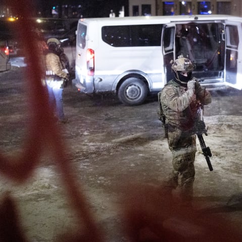 Several federal agents and their van is seen through a window at night.