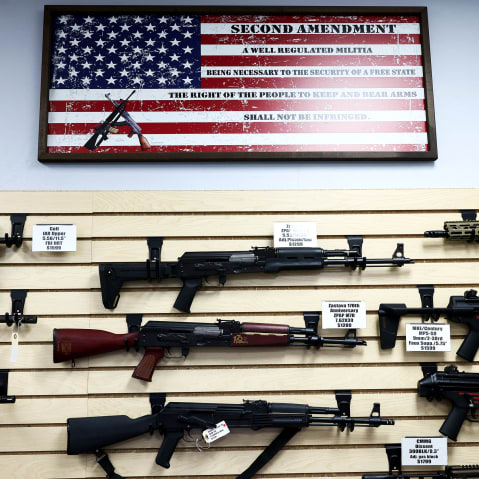 A bunch of weapons are on display below a US flag at a gun store.