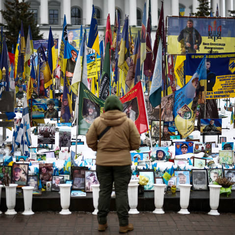 A person stands in front of photos and flags in a memorial.