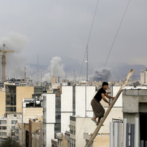 There is a man climbing up stairs while there is smoke rising inthe skyline of Tehran in the background.