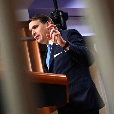 Todd Blanche is seen through two white bars as he speaks at a presser.