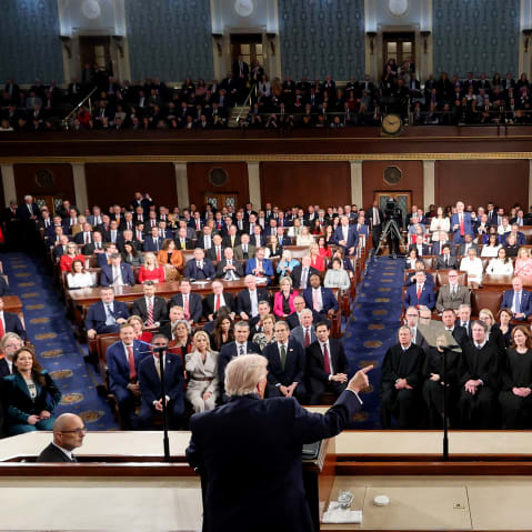 Donald Trump is seen from behind as he speaks to the congress during his SOTU. Members of the congress fill the majority of the frame as they listen to him.