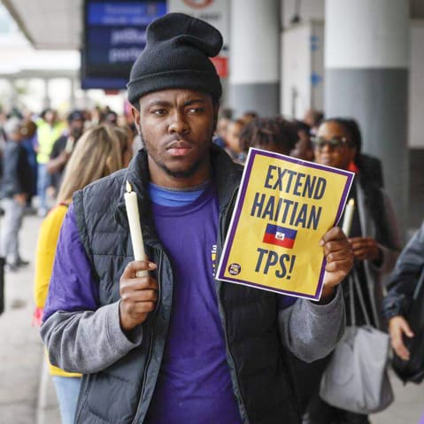 A man holds a candle and a sign about [protection tps for Haitians.
