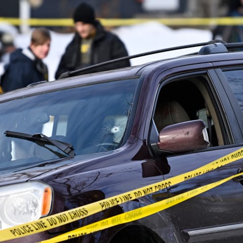 A car with a bullet hole in the windshield surrounded by yellow police tape.