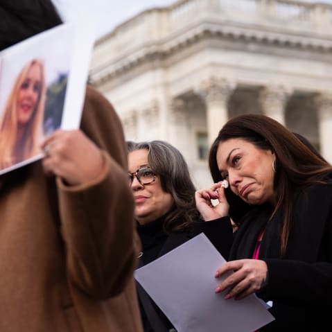 Epstein survivor Haley Robson, second from right, wipes tears from her eyes with tissue. She is surrounded by people, including other survivors.