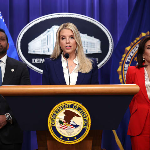 Pam Bondi speaks at the podium while Kash Patel and Jeanine Pirro stand behind her.