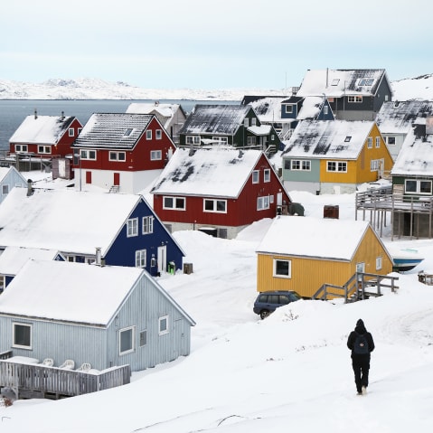 A man walks through the snow towards residential houses in Nuuk, Greenland.