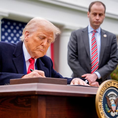 President Trump signs a document at his desk about imposing tariffs.