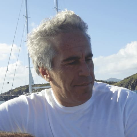 Jeffrey Epstein is looking down on the ocean while the shore and another boat can be seen in the background.