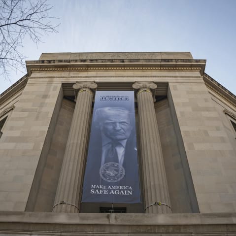 A blue banner with the slogan "Make America Safe Again" and a photo of Donald Trump hangs on the facade of the Department of Justice.