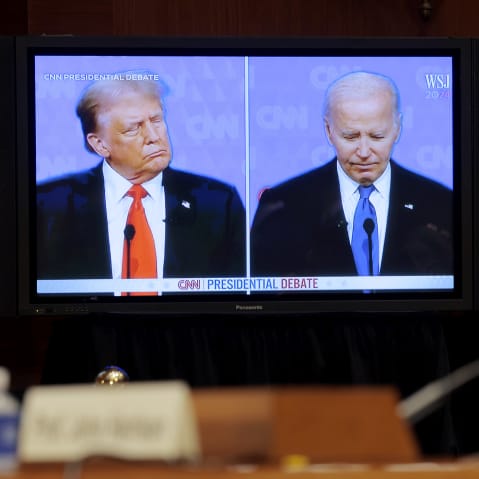 Donald Trump and Joe Biden are seen on a split screen while there is a man sitting in front of the screen to the right of the frame, out of focus.
