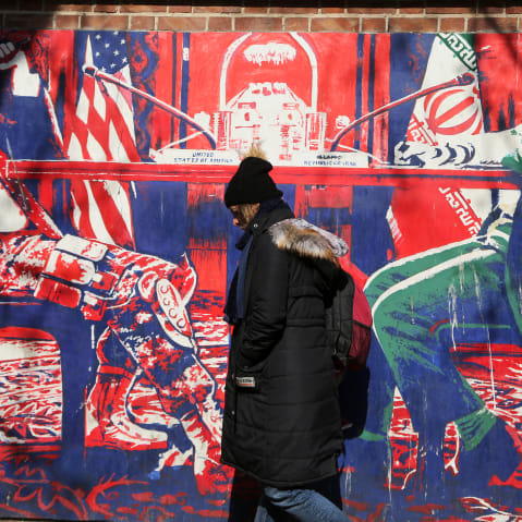 A woman walks by a red and blue mural that sends an anti-american message.