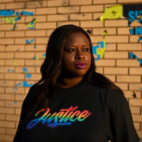 Nekima Levy Armstrong, wearing a shirt that says "justice" in rainbow letters, poses in front of a brick wall.