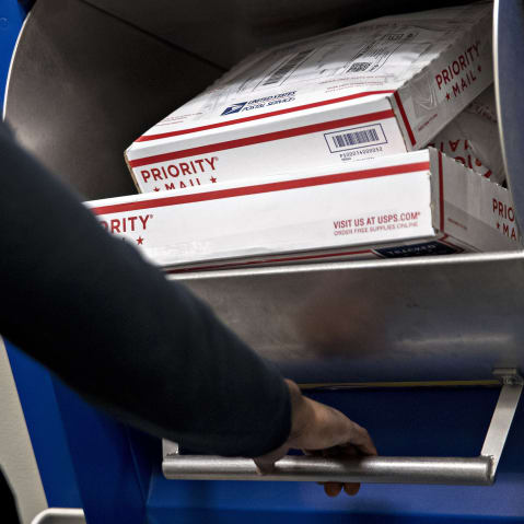 A customer places United States Postal Service (USPS) priority mail packages into a drop-off bin.