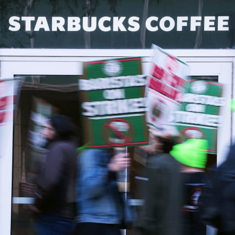 People blurred in motion hold signs in front of a Starbucks Coffee location.