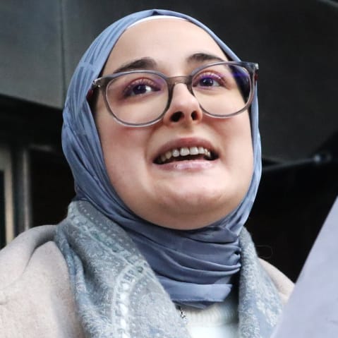 Rumeysa Ozturk speaks to press outside a courthouse. The photo is a tight frame and shot from below.