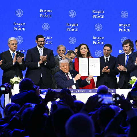 Presidents, prime ministers, and other leaders from around the world surround Donald Trump, who holds a signed charter. Audience members in the foreground take pictures.