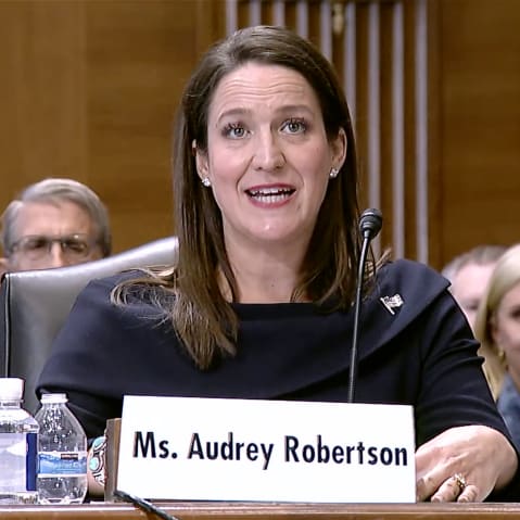 Audrey Robertson sitting at a table with a microphone behind a name tag.