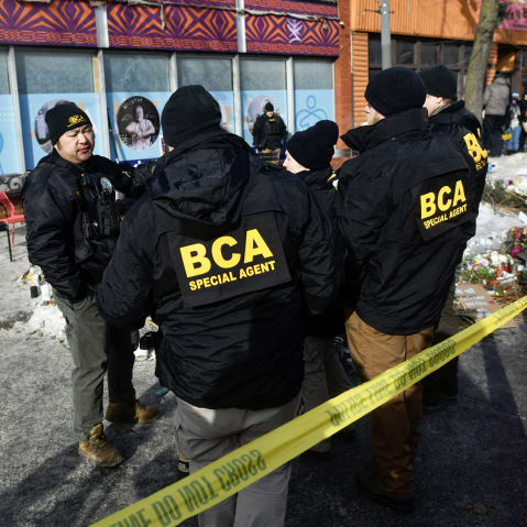 Bureau of Criminal Apprehension police officers survey the scene near a makeshift memorial in the area where Alex Pretti was shot dead a day earlier by federal immigration agents.