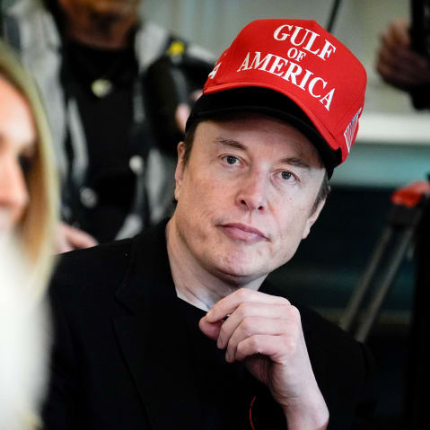 Elon Musk looks on while wearing a red Gulf of America cap over his black cap.