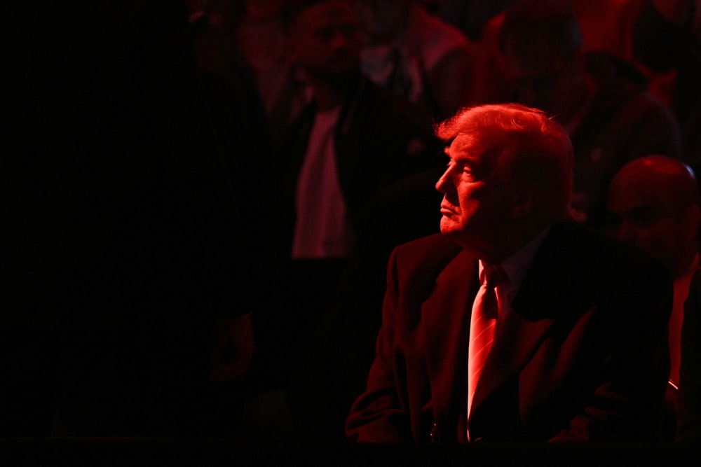 Donald Trump looks into the distance. He and the crowd are basked in red light.